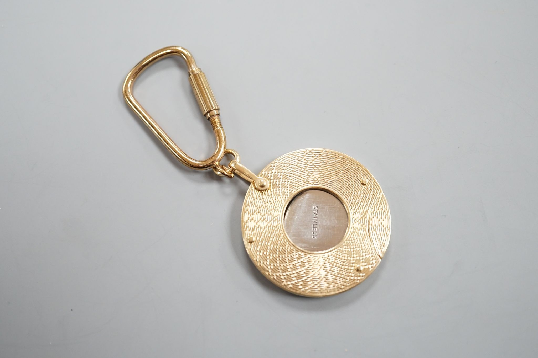 A 1960's engine turned 9ct gold mounted circular cigar cutter, 34mm, with gilt metal fob clip.